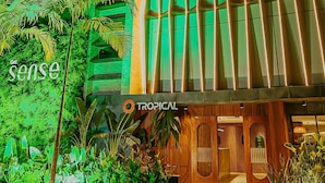 A modern building with a green-lit facade, a tropical-themed entrance, and the words 'sense' and 'tropical' visible. - Get Sense Beira Mar (Joao Pessoa)