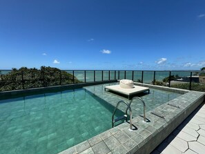 A rooftop infinity pool with clear water, a lounge chair, and a view of the ocean. - Get Sense Beira Mar (Joao Pessoa)