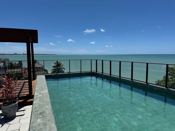 A clear view of a swimming pool with a metal railing, potted plants, and a wooden pergola. - Get Sense Beira Mar (Joao Pessoa)