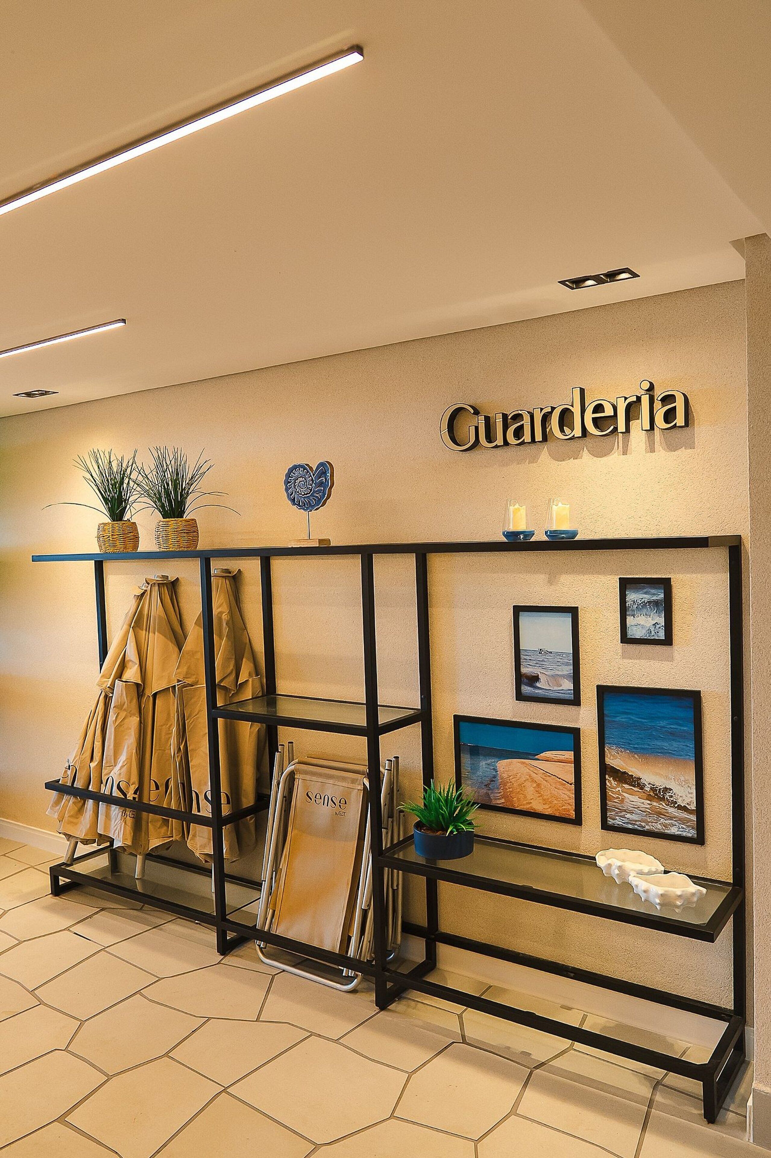 A hotel reception area with a name sign, a shelf with plants, coats, and framed pictures.