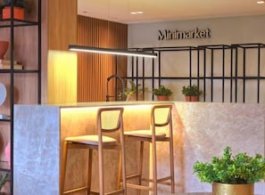 A reception area with a marble counter, two bar stools, a potted plant, and a 'Minimarket' sign. - Get Sense Beira Mar (Joao Pessoa)