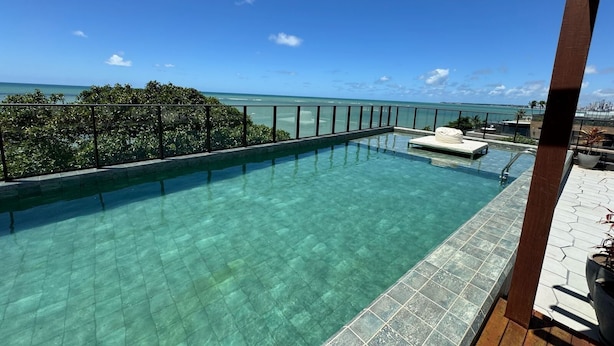 A clear swimming pool with a view of the ocean and a city skyline in the background. - Get Sense Beira Mar (Joao Pessoa)