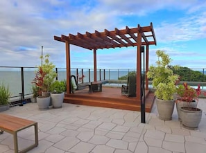A covered outdoor seating area with a wooden pergola, potted plants, and a view of the sea. - Get Sense Beira Mar (Joao Pessoa)