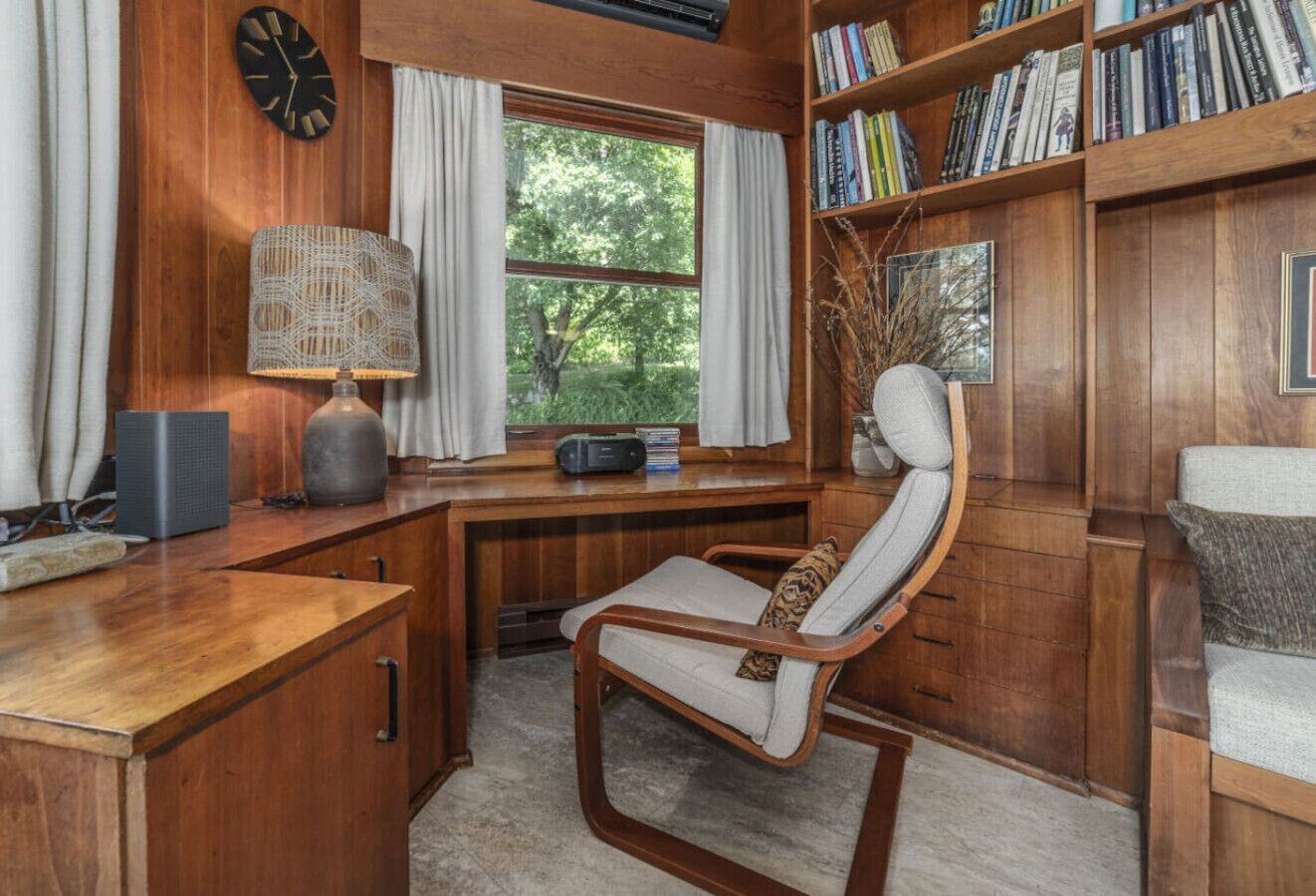 Una habitación acogedora con un escritorio de madera, una silla cómoda, una estantería y una ventana con cortinas.