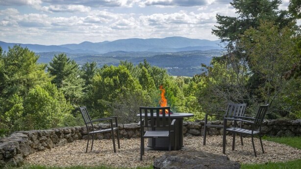 A stone fire pit with two chairs and a table, surrounded by a stone wall and a grassy area with trees and mountains in the background. - Secluded Mid-Century Retreat w/ mtn views, near WLU, VMI (Rockbridge County)