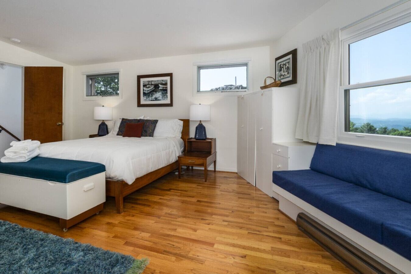 Een slaapkamer met een bed, nachtkastje, kledingkast, bank en raam met uitzicht.