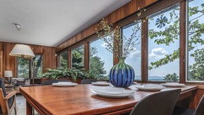 A dining area with a wooden table set for four, large windows, and a vase with branches. - Secluded Mid-Century Retreat w/ mtn views, near WLU, VMI (Rockbridge County)