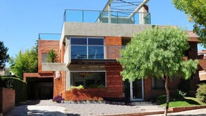 Une maison moderne à deux étages, dotée d’un balcon en verre, d’une façade en briques et d’un jardin bien entretenu.