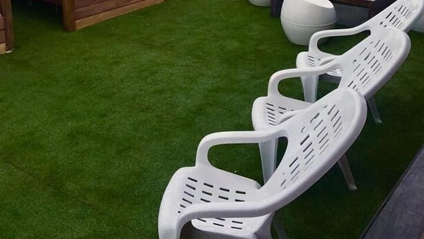 Une terrasse dotée d’une pergola en bois, d’une petite table et de chaises en plastique blanches.
