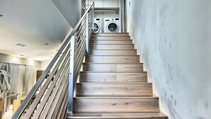 A modern staircase with wooden steps and metal railings, leading to a laundry area with two washing machines. - 𝐵𝑒𝒶𝓊𝓉𝒾𝒻𝓊𝓁 Townhouse Haven from Hollywood—with PRIVATE BALCONY VIEW (Los Angeles)