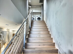 Un escalier moderne avec des marches en bois et des rampes en métal, menant à une buanderie équipée de deux machines à laver.