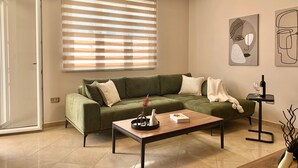 Un salon avec un canapé vert, une table basse en bois et une petite table d’appoint sur laquelle se trouvent une bouteille de vin et des verres.