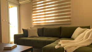 Un salon avec un canapé vert, un plaid blanc et une table basse en bois.