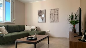Un salon avec un canapé vert, une table basse en bois et deux œuvres d’art abstraites accrochées au mur.