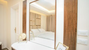 A modern bedroom with a large mirror, a bed with white linens, a wooden headboard, and a view of another room through the mirror.