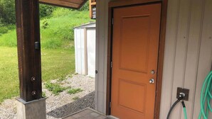A wooden door with a metal handle, a metal post, and a green hose attached to the wall.