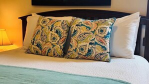A bed with a patterned pillow, a plain pillow, and a teal throw blanket.