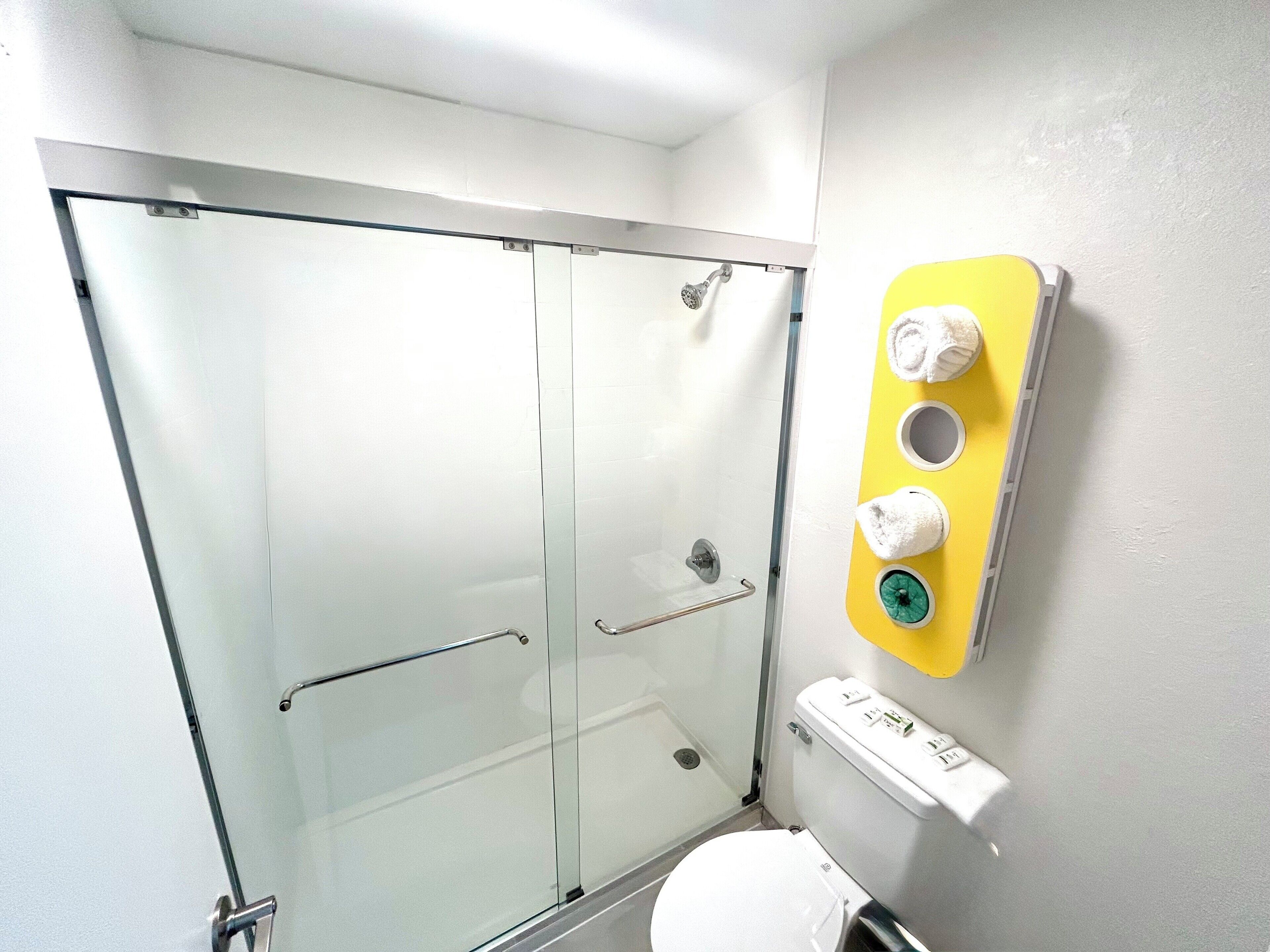 A bathroom with a glass shower enclosure, a toilet, and a wall-mounted towel warmer with two towels.