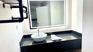 Ein Badezimmer mit weißem Waschbecken, einem Spiegel und einer schwarzen Ablagefläche.