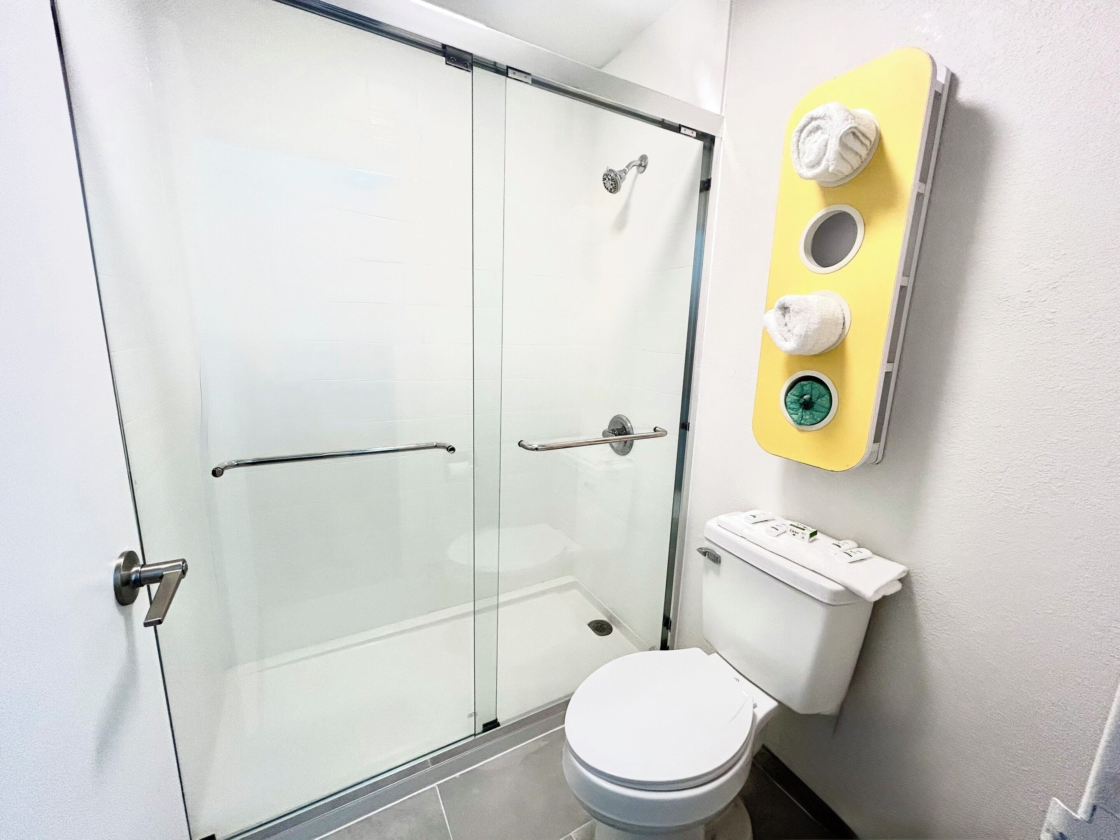 A modern bathroom with a glass shower enclosure, a toilet, and a towel rack with two towels.
