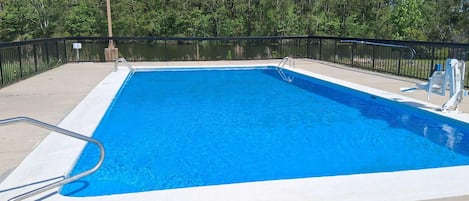 A rectangular swimming pool with a metal ladder on one side, surrounded by a black metal fence.