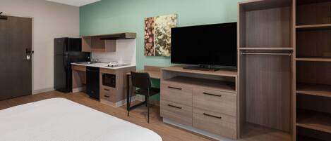 Ein modernes Hotelzimmer mit einem großen Bett, einer Küchenzeile, einem Fernseher und einem Kleiderschrank.