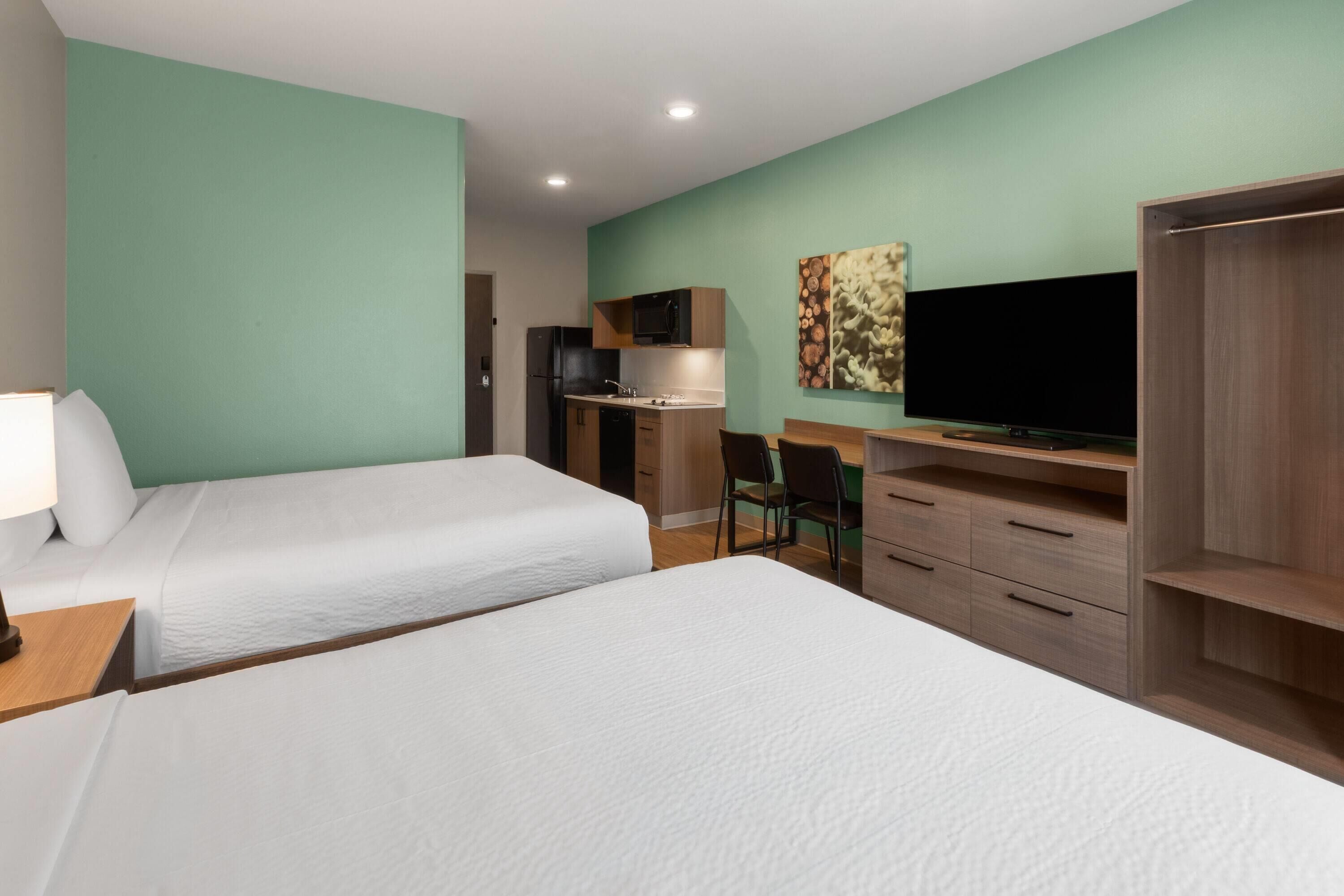A hotel room with two beds, a desk with a flat-screen TV, a microwave, and a cabinet.