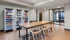 A conference room with a long table, four white chairs, and three beverage vending machines.