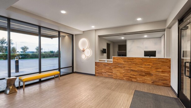 A modern reception area with a wooden reception desk, a bench, and a large window offering a view of the parking lot.