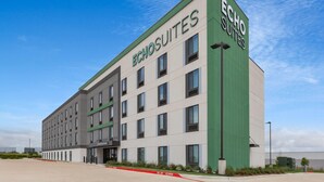 A modern hotel building with 'ECHO SUITES' signage, a flat facade, and a parking area with red curbs.