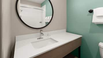 Un baño con un lavamanos blanco, un espejo redondo y un inodoro.