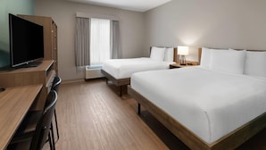A hotel room with two beds, a desk, a TV, and a window with curtains.