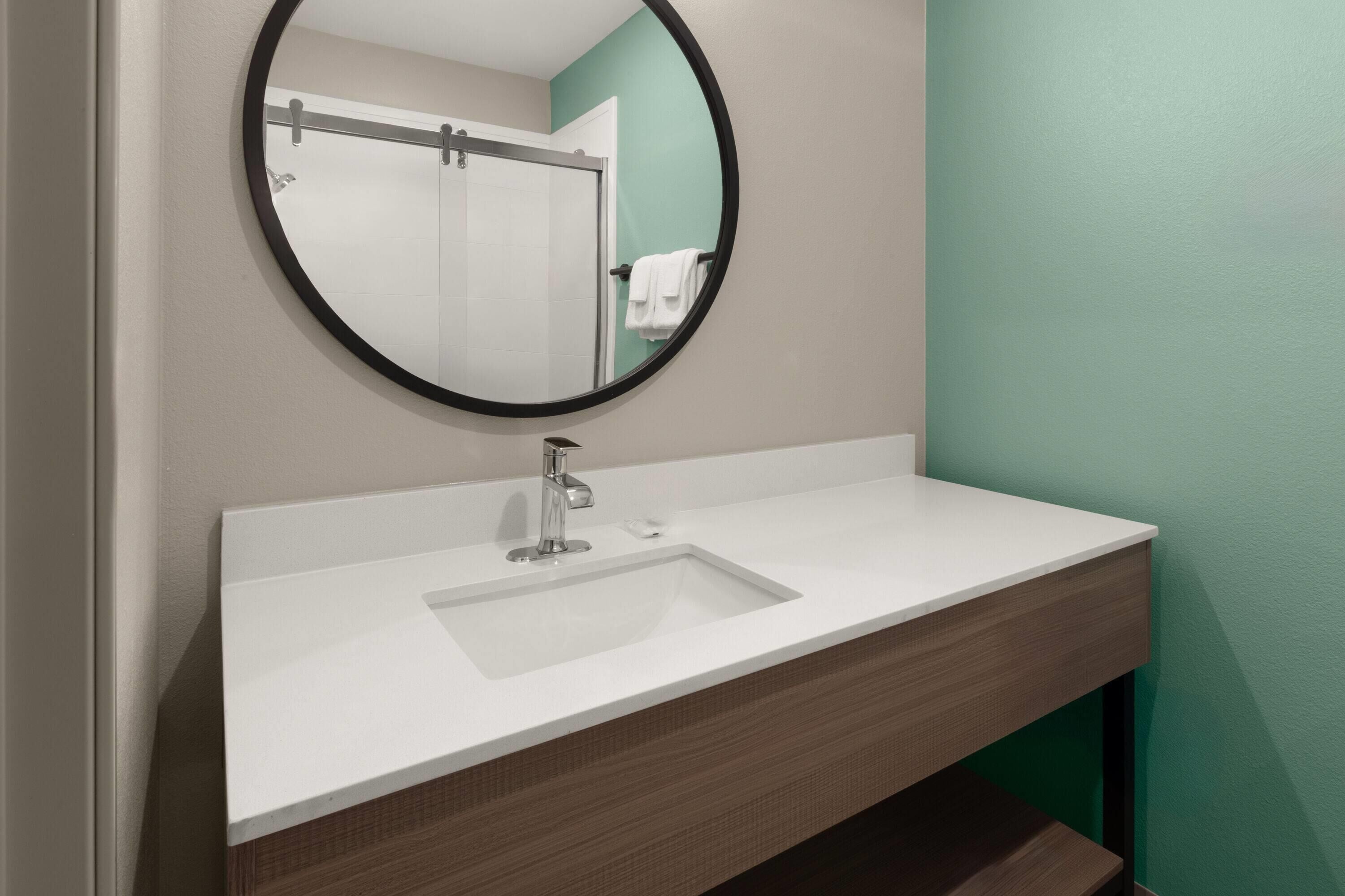 Een badkamer met een wit wastafelmeubel, een ronde spiegel en een groene wand.