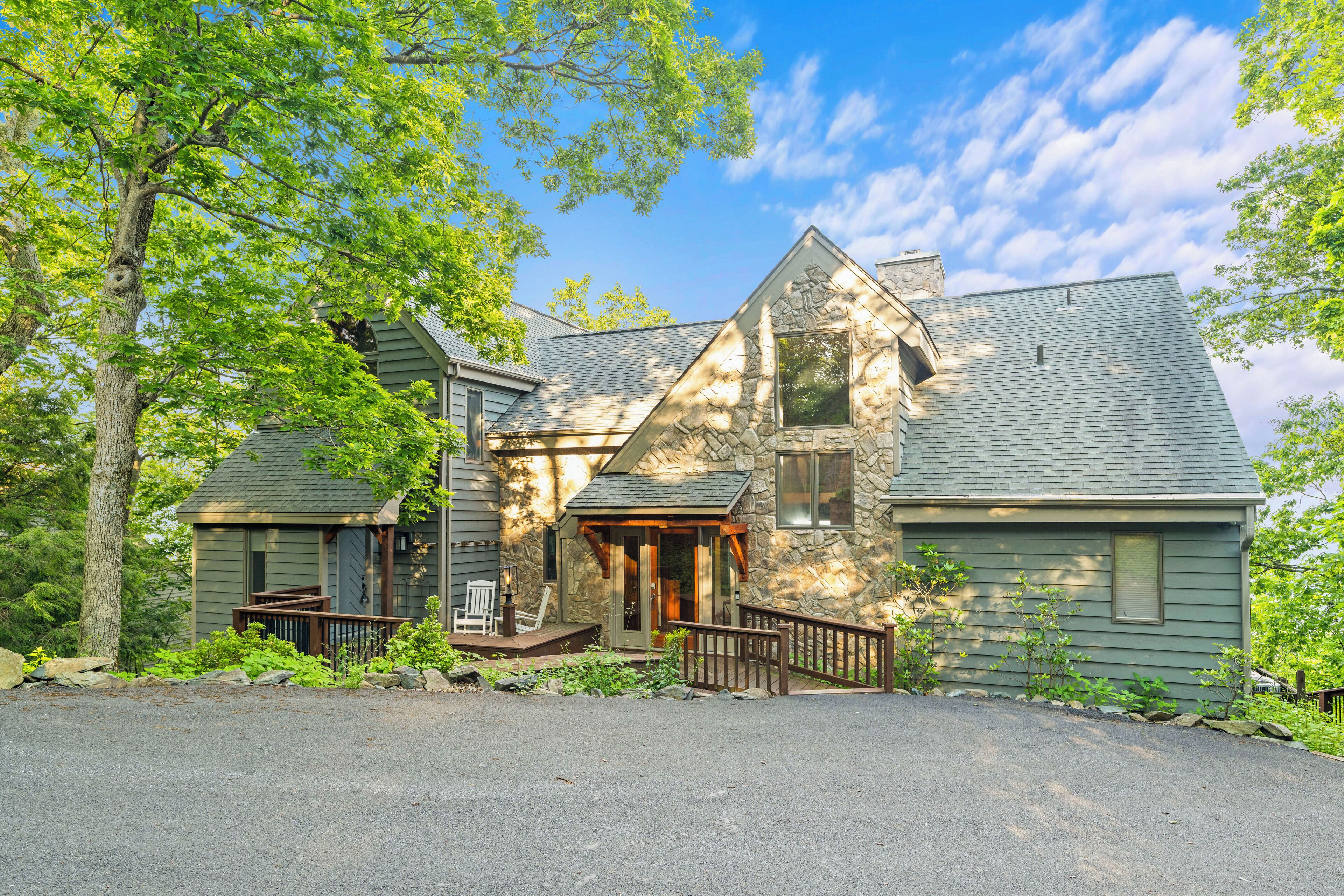 A two-story stone house with a stone chimney, a front porch, and a small deck.
