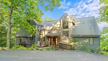 A two-story stone house with a stone chimney, a front porch, and a small deck.