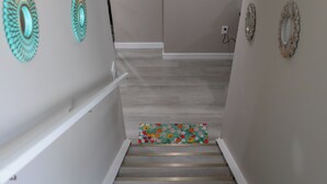 A staircase with a wooden handrail, a floral-patterned rug at the bottom, and decorative wall mirrors. - Cozy 2BR/2BA Suite | 10 Mins to Airport | Private Entry & Kitchen (Calgary)