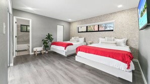 Quarto moderno com duas camas, um banheiro pequeno e uma TV na parede.