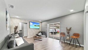 Uma sala de estar moderna com um sofá cinzento, uma mesa de centro e uma TV na parede.