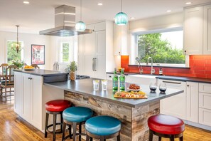 A modern kitchen with a large island, bar stools, and a window providing a view of greenery outside.