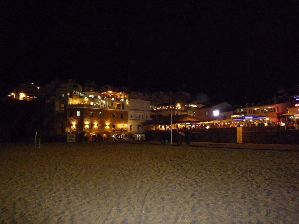 Et strandhotel med flere etager, udendørs siddeområder og en sandstrand i forgrunden.