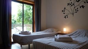 Une chambre d’hôtel avec deux lits, une grande fenêtre avec des rideaux, une plante décorative fixée au mur et une lampe de chevet.