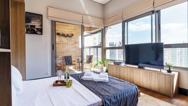 Una camera d'albergo moderna con un letto grande, una televisione a schermo piatto, un balcone con vista sulla città e un muro in mattoni a contrasto.
