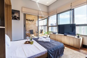 A modern hotel room with a large bed, a flat-screen TV, a balcony with a city view, and a brick accent wall. - Perto do Allianz Park com Piscina e AC (Sao Paulo)