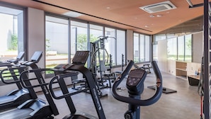 Una palestra moderna con macchinari cardio, attrezzature per allenamento con i pesi e ampie finestre che offrono vista sull'esterno.