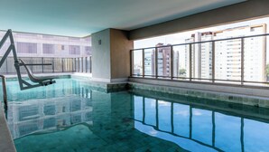 Una piscina interna con acqua cristallina, un trampolino e vista su grattacieli attraverso ampie finestre.