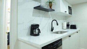 A modern kitchen with white countertops, a black coffee maker, a sink, and a potted plant. - Spacious 2-Bed-Room near Yonge & Major Mackenzie (Richmond Hill)