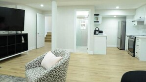 A modern living room with a flat-screen TV, a leopard print sofa, and a kitchen area with white cabinets and appliances. - Spacious 2-Bed-Room near Yonge & Major Mackenzie (Richmond Hill)
