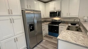 Una cocina moderna con armarios blancos, electrodomésticos de acero inoxidable, horno empotrado y encimera de granito.