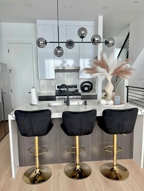 A modern kitchen with white cabinets, a central island with three black bar stools, and pendant lights above the island. - LuxeStay Townhome 5min from Downtown Dallas (Dallas)