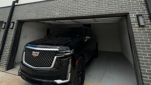 A modern building with a garage entrance, a black SUV parked inside, and a brick facade. - LuxeStay Townhome 5min from Downtown Dallas (Dallas)